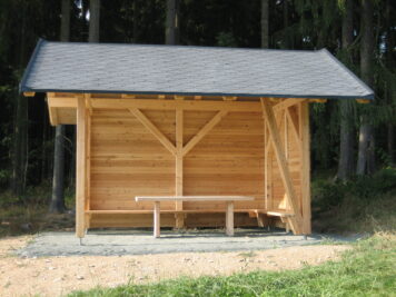 Holzbau der Tischlerei Holzwelten Schlosser GmbH – Handwerk aus Oelsnitz für Wanderer und Naturfreunde Schutzhütte aus Holz mit Sitzbank am Wanderweg „Vogtländischer Knollensteig“, gebaut von der Tischlerei Holzwelten Schlosser GmbH aus Oelsnitz