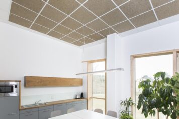 Nachhaltige Akustikpaneele aus Holzfasern, Lehm und Schafwolle für gesunde Raumluft und modernes Design CLIMAPANEEL Schallabsorber in Rasterdecke einer modernen Küche mit Holz- und Weißelementen, verbessert Raumakustik und Raumklima