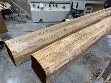 Massive Balken aus Holz mit sichtbarer Maserung, vorbereitet für den weiteren Einsatz Zwei massive Holzbalken mit bearbeiteter Oberfläche liegen in einer Werkstatt auf Böcken, im Hintergrund sind Maschinen und Holzspäne erkennbar.