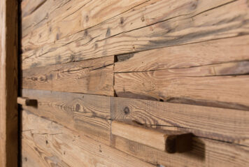 Individuelle Oberflächengestaltung aus historischem Holz – gefertigt von Holzwelten Schlosser GmbH, Oelsnitz Nahaufnahme einer strukturierten Altholz-Wandverkleidung aus massiven, unregelmäßig aufbereiteten Holzlamellen in verschiedenen Naturtönen.