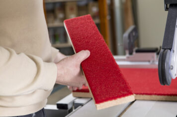 Präziser Zuschnitt eines Climapaneels mit roter Filzoberfläche in der Werkstatt in Oelsnitz. Handwerklicher Zuschnitt eines Climapaneels mit roter Filzoberfläche an einer Tischkreissäge in der Werkstatt der Tischlerei Holzwelten Schlosser in Oelsnitz.