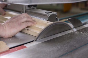 Präziser Zuschnitt eines Climapaneels mit roter Filzoberfläche in der Werkstatt in Oelsnitz. Handwerklicher Zuschnitt eines Climapaneels mit roter Filzoberfläche an einer Tischkreissäge in der Werkstatt der Tischlerei Holzwelten Schlosser in Oelsnitz.