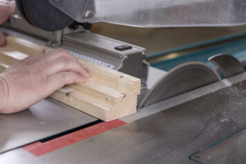 Präziser Zuschnitt eines Climapaneels mit roter Filzoberfläche in der Werkstatt in Oelsnitz. Handwerklicher Zuschnitt eines Climapaneels mit roter Filzoberfläche an einer Tischkreissäge in der Werkstatt der Tischlerei Holzwelten Schlosser in Oelsnitz.