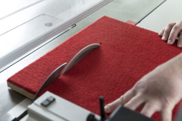 Präziser Zuschnitt eines Climapaneels mit roter Filzoberfläche in der Werkstatt in Oelsnitz. Handwerklicher Zuschnitt eines Climapaneels mit roter Filzoberfläche an einer Tischkreissäge in der Werkstatt der Tischlerei Holzwelten Schlosser in Oelsnitz.