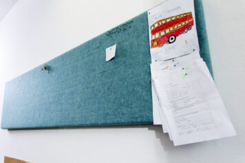 Akustik, Raumklima und Organisation – natürlich vereint Türkises Climapaneel aus Schafwollvlies, genutzt als Pinnwand mit Zetteln und einer Kinderzeichnung, handgefertigt von Holzwelten Schlosser in Oelsnitz.