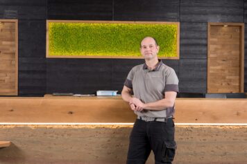 Empfangstresen aus Stampflehm mit indirekt beleuchteter Mooswand und natürlichen Holzoberflächen. tresen stampflehm mooswand indirekte beleuchtung