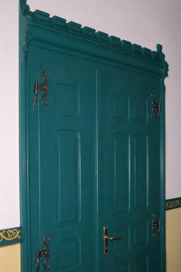 Nach historischem Vorbild gefertigte Innentür aus Massivholz mit traditionellen Verzierungen und handwerklichen Details. Historische Innentür aus Massivholz mit profilierter Zarge, dekorativen Beschlägen und aufwendig gestaltetem Kapitell nach historischem Vorbild.